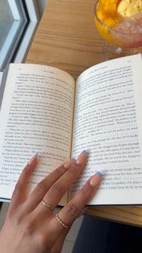 a woman's hand holding a book and a bowl of fruit